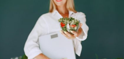 A woman with a vibrant smile offering a fresh salad bowl, promoting healthy eating.