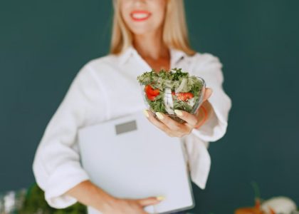 A woman with a vibrant smile offering a fresh salad bowl, promoting healthy eating.