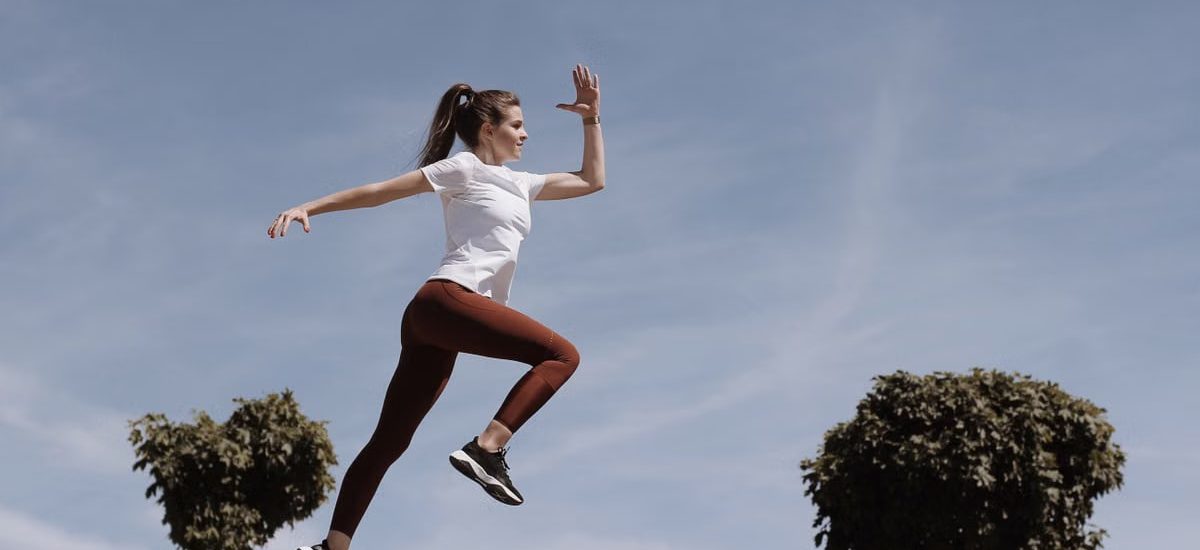 Athletic woman in action jump against a blue sky background. Captures fitness in motion.