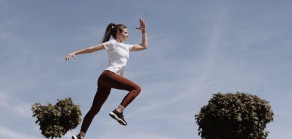 Athletic woman in action jump against a blue sky background. Captures fitness in motion.