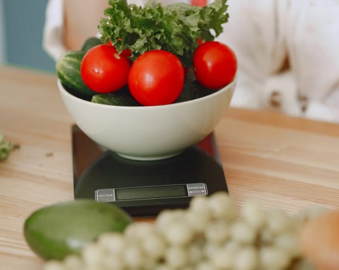 Colorful fresh vegetables including tomatoes and cucumbers on a kitchen scale for healthy eating.