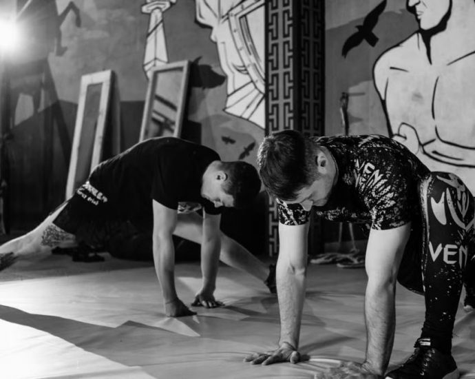 Two men stretching inside a gym, preparing for MMA training in a grayscale setting.