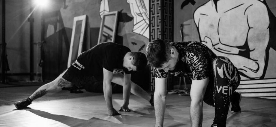 Two men stretching inside a gym, preparing for MMA training in a grayscale setting.